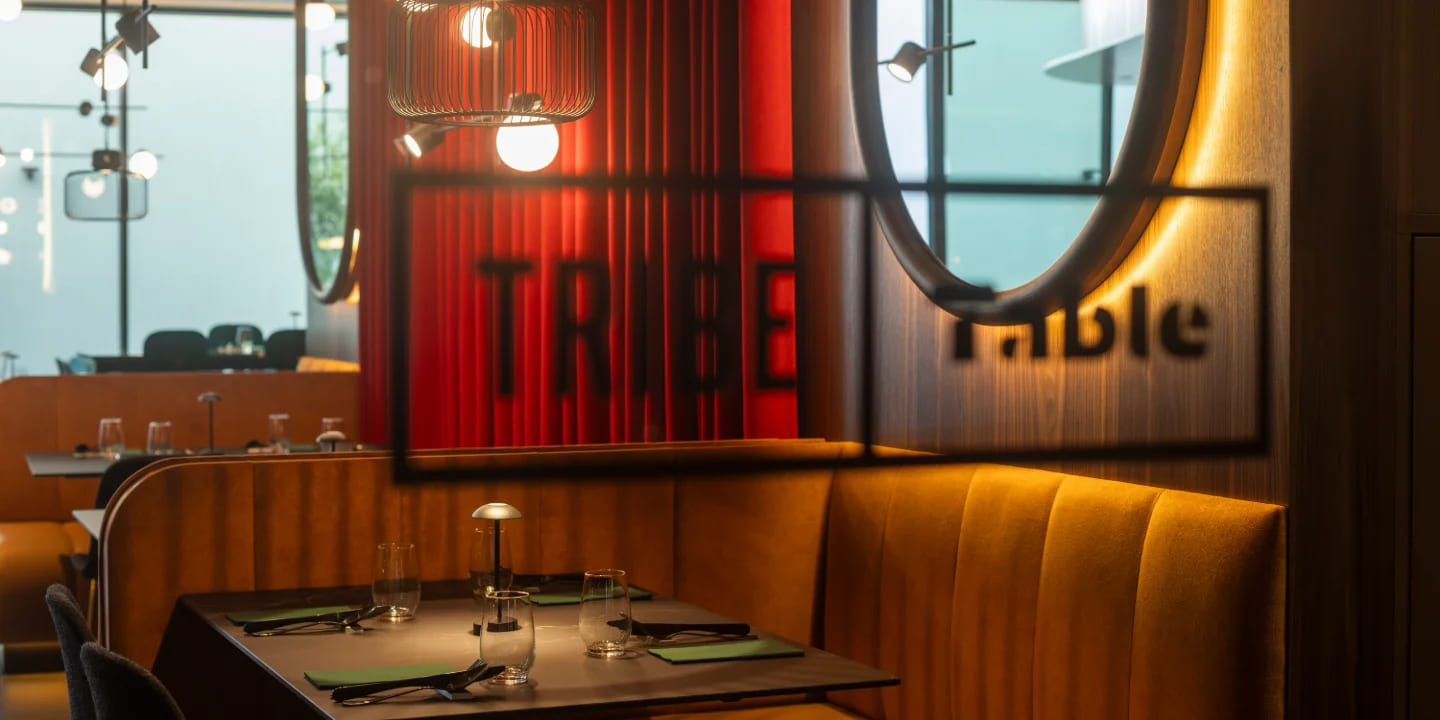 Cozy restaurant scene featuring modern decor, illuminated seating, and a prominent "TRIBE" sign casting a shadow on a wooden wall.