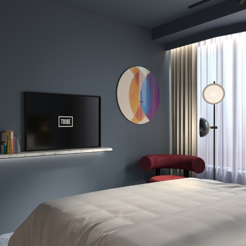 Modern hotel room featuring a double bed, wall-mounted TV with "TRIBE" logo, colorful wall art, and a cozy red accent chair.