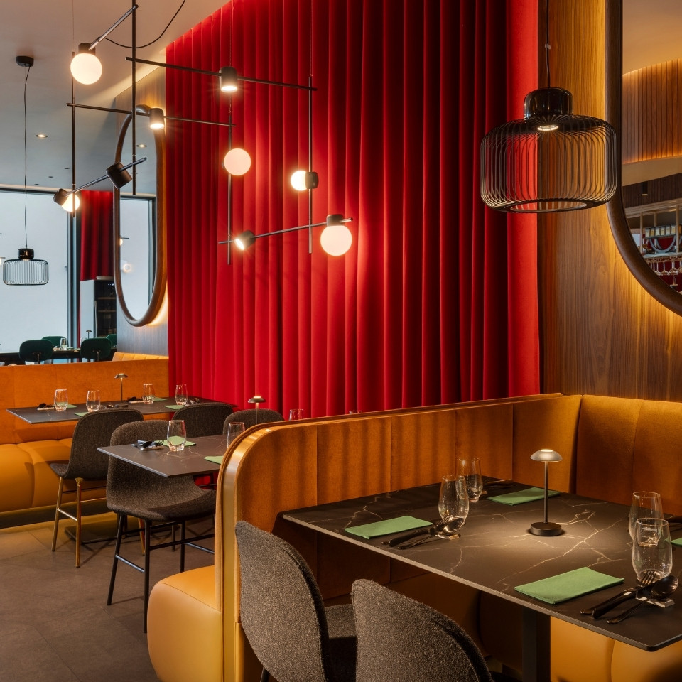 Stylish restaurant interior featuring red velvet walls, modern lighting, and plush seating with elegantly set tables.