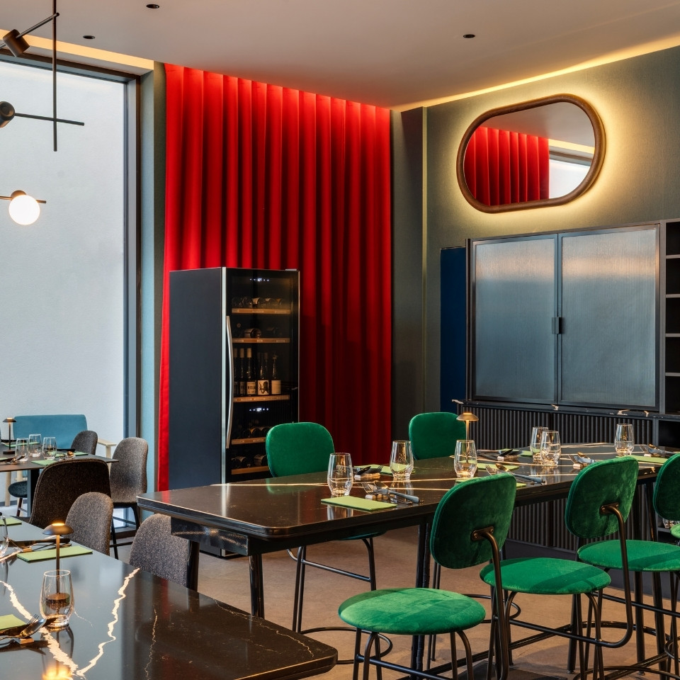 A modern dining room featuring green velvet chairs, a sleek black table, and a striking red curtain backdrop.