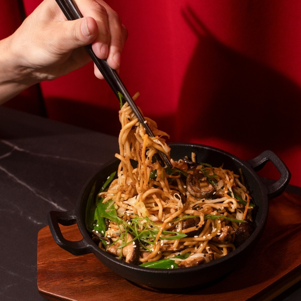 A person using chopsticks to pick up noodles from a bowl, showcasing a traditional Asian dining experience.