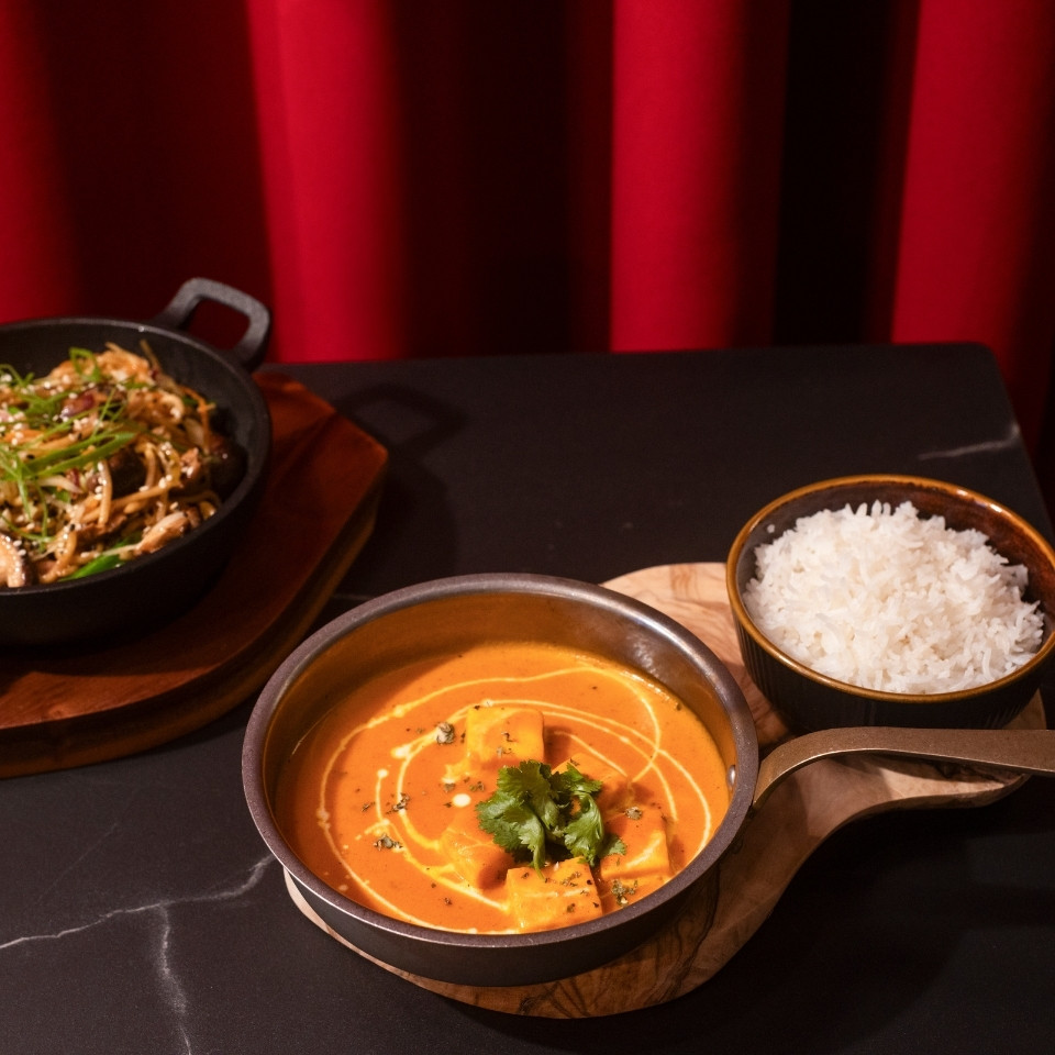 Two bowls of food sit on a table, with a vibrant red curtain draping in the background.