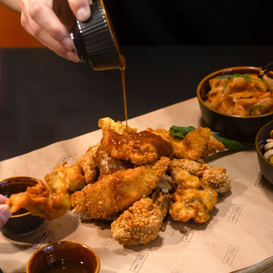 A person pouring sauce over fried chicken and various side dishes on a dining table.