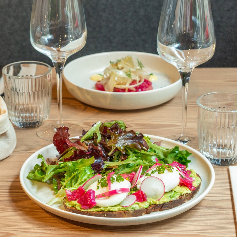 on a plate is a bread with avocado, salad and different toppings