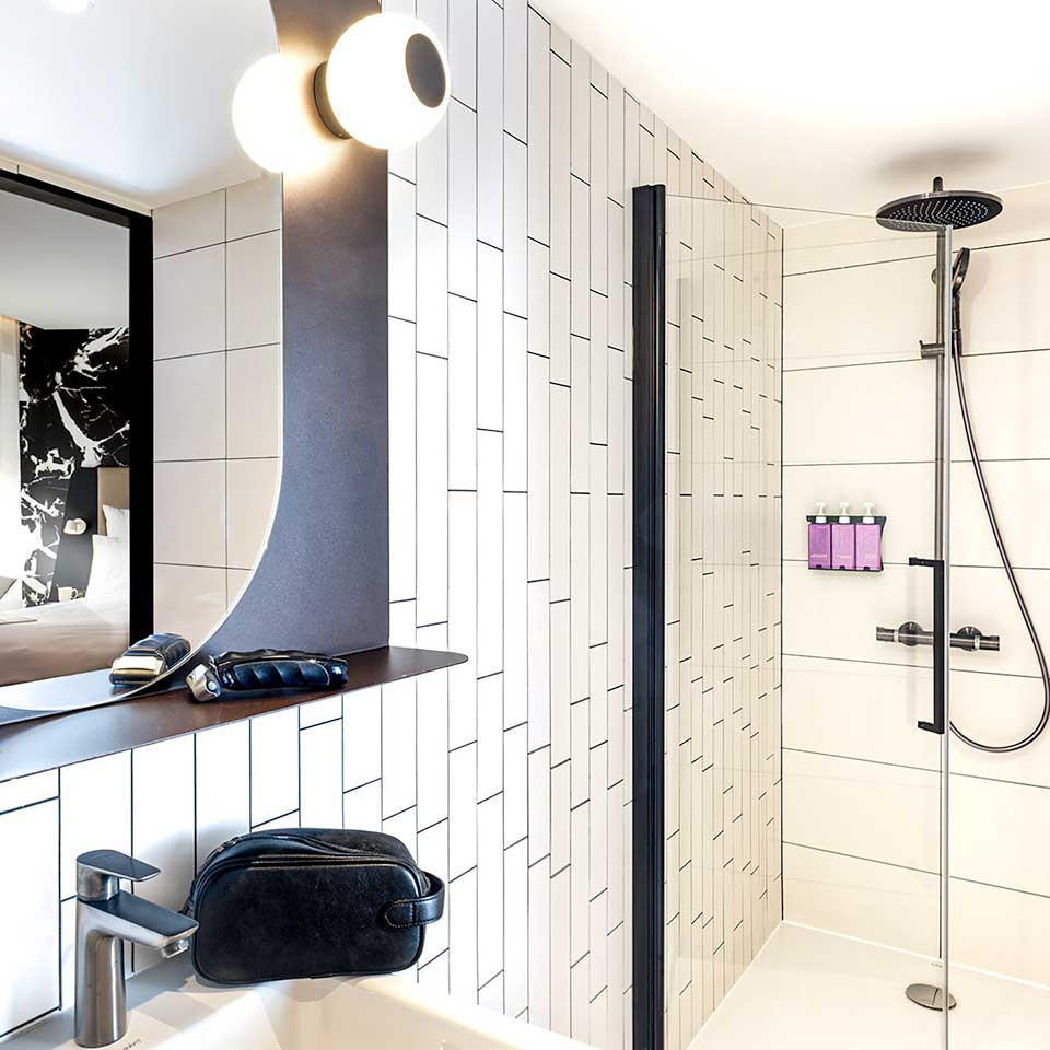 White tiled backroom with rain shower with bedroom reflected in make-up mirror