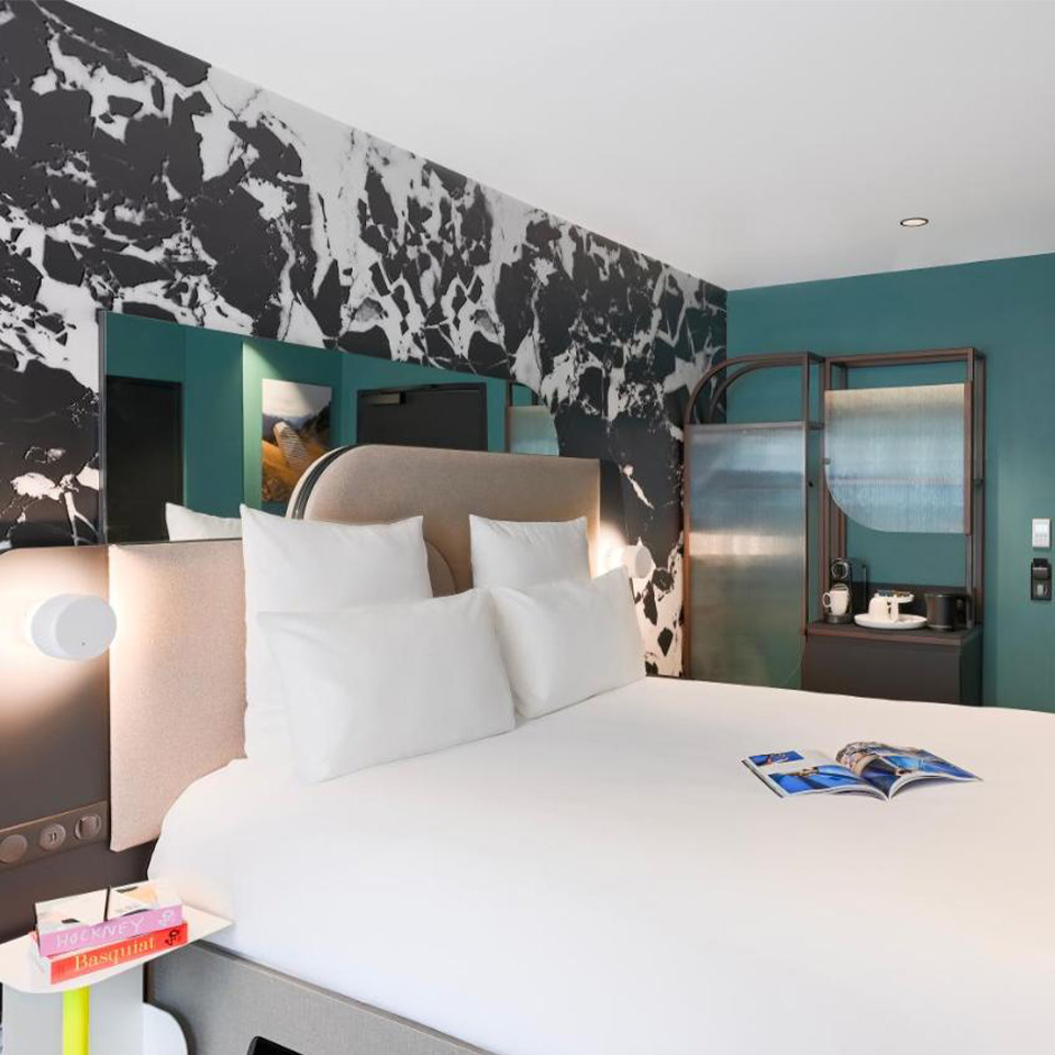 Hotel room with double bed, side table, coat rack and small desk with coffee machine