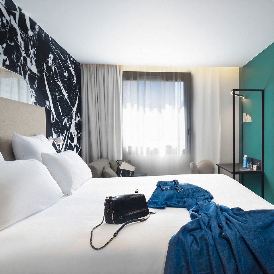 Hotel room with dress and handbag laying on double bed, sofa bed and small desk.