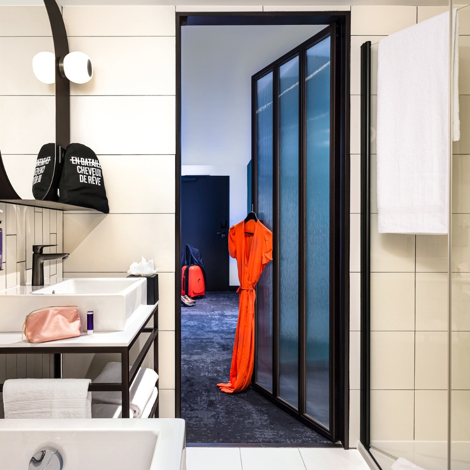 A modern bathroom with a bathtub, sink, and an orange dress hanging by a frosted glass door, leading to a stylish room beyond.