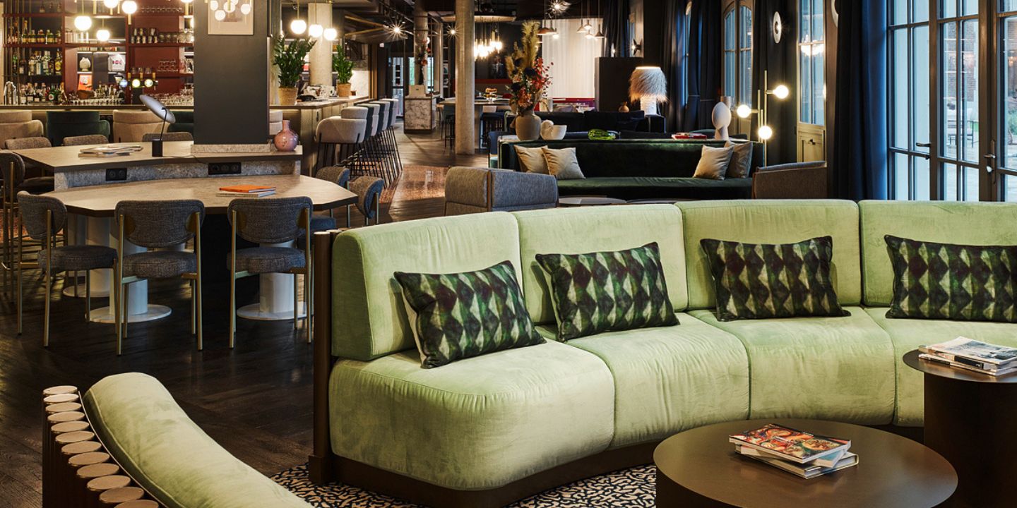 A large green couch with pillows in a common area with several tables and chairs