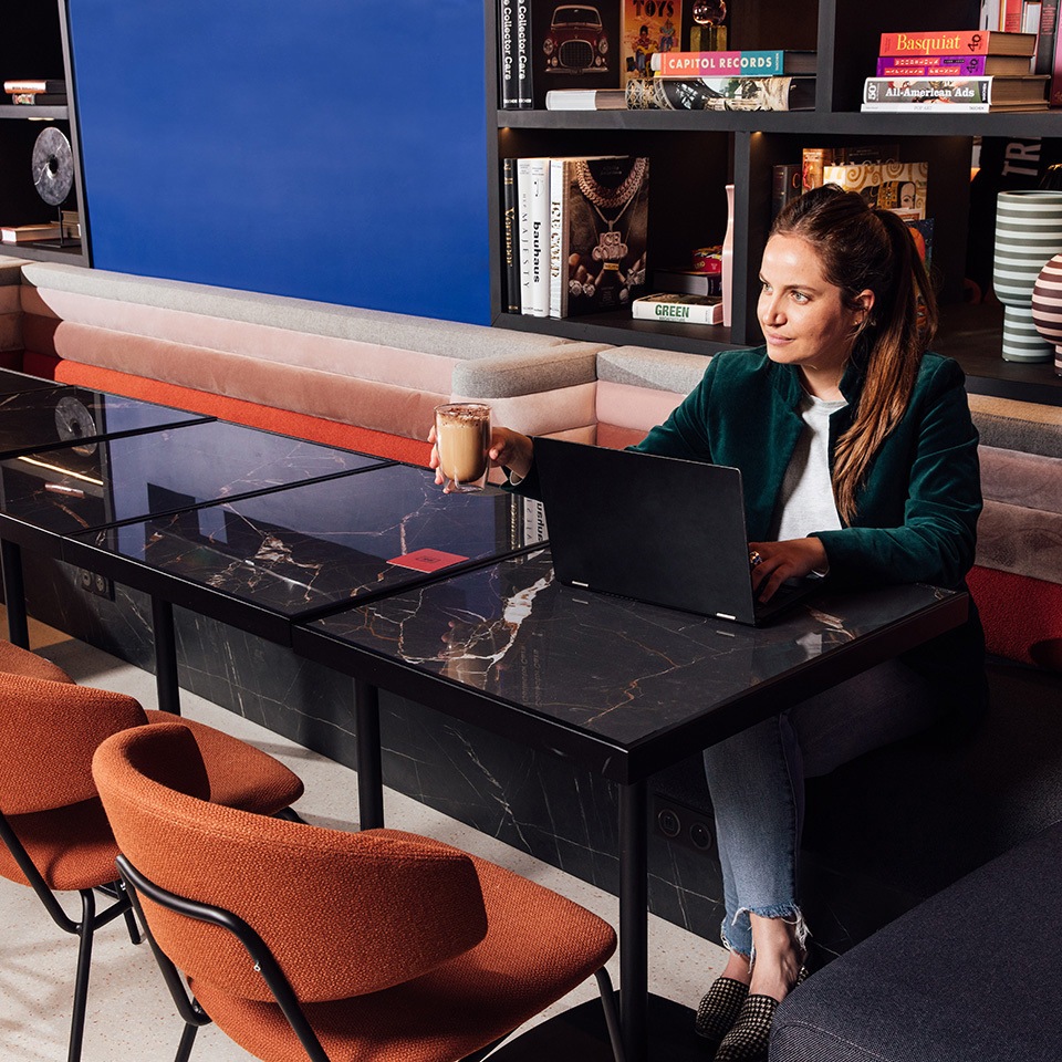 A person sits at a stylish marble-topped table, working on a laptop and enjoying a drink in a cozy, modern workspace.