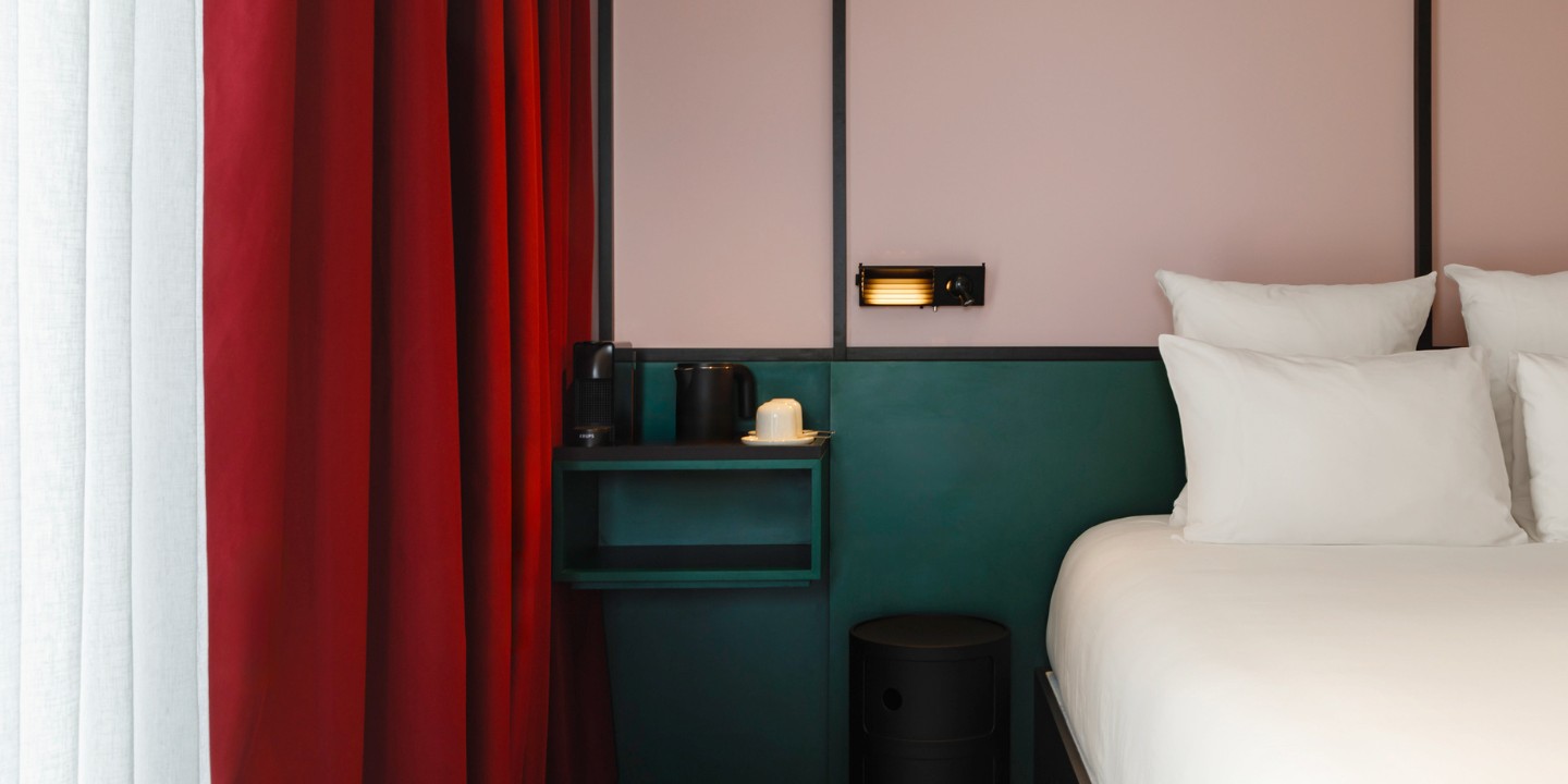 a hotel room in TRIBE Lyon, the walls are two-toned with a dark turquoise on the bottom and a light pink at the top, the curtains are red