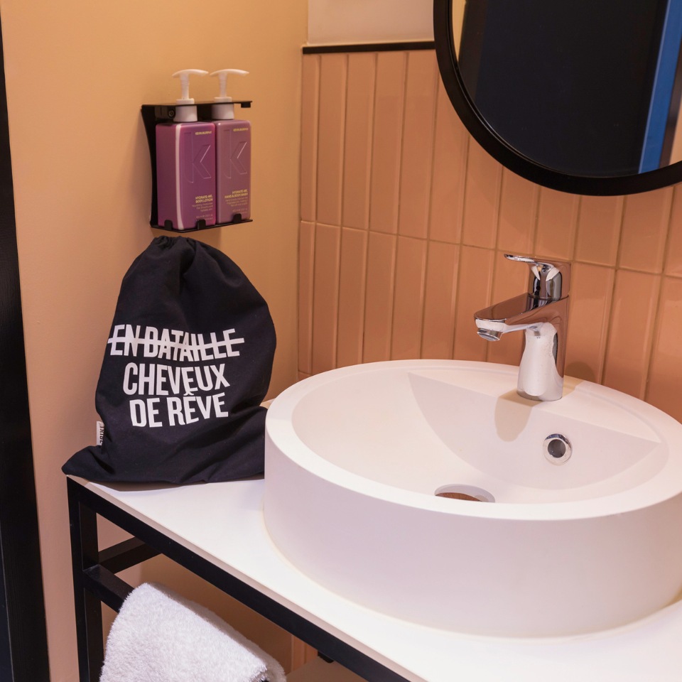 A modern bathroom with a round sink, a black bag with a hairdryer and shampoo dispensers on the wall.