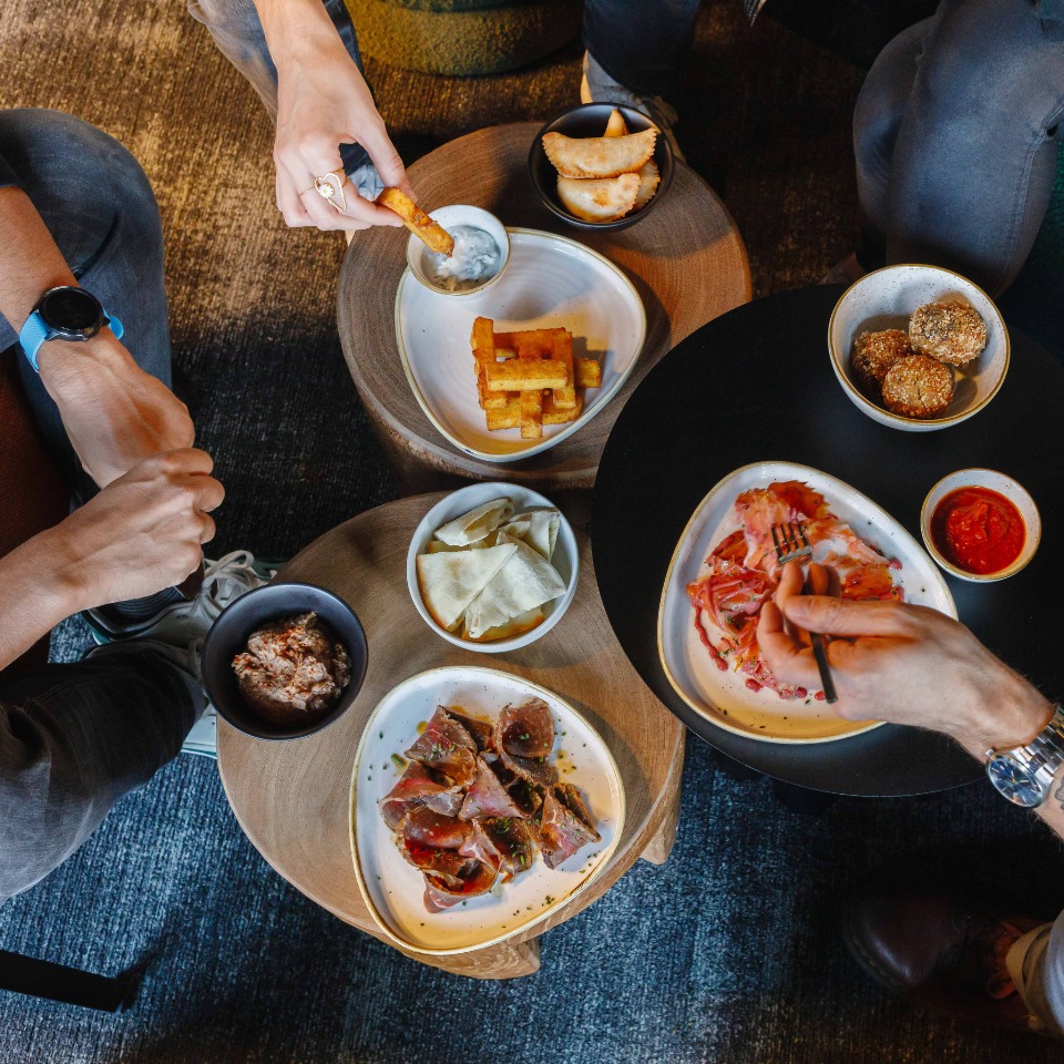 A top-down view of shared appetizers, including meats, fries, dips, and chips, with hands reaching for the food in a cozy setting.