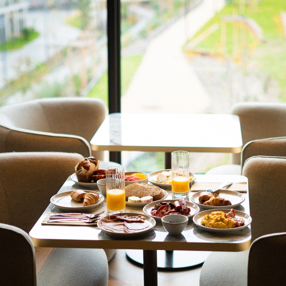 A beautifully arranged breakfast spread on a table, featuring croissants, eggs, bacon, toast, fresh fruit, and orange juice.