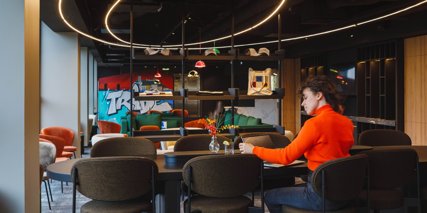 A modern cafe interior featuring stylish seating, vibrant art on the walls, and warm lighting from a circular fixture above.