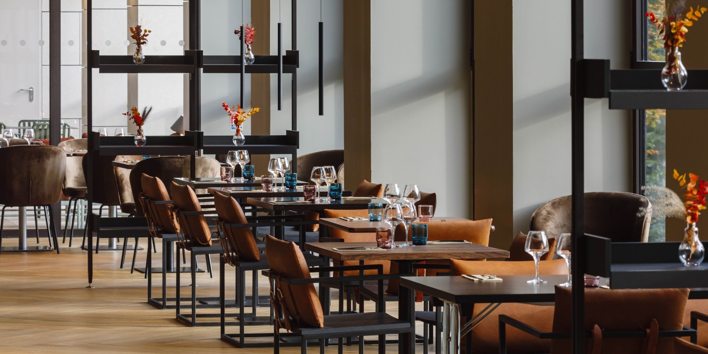 view into the restaurant with chairs with orange cushions and square tables, on the tables are glasses