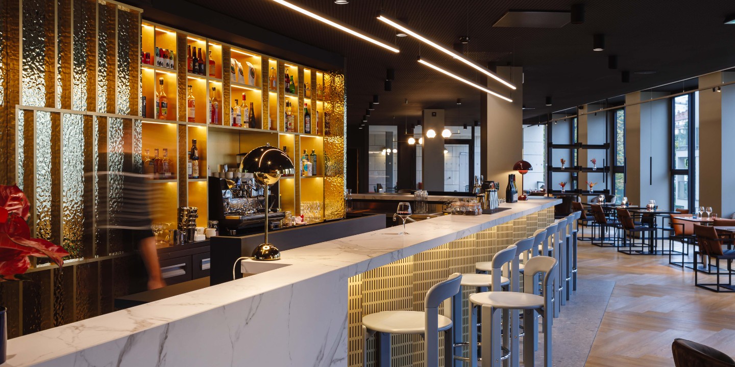 the bar at TRIBE Lyon, a marble counter and white highchairs. in the background is a well equipped bar