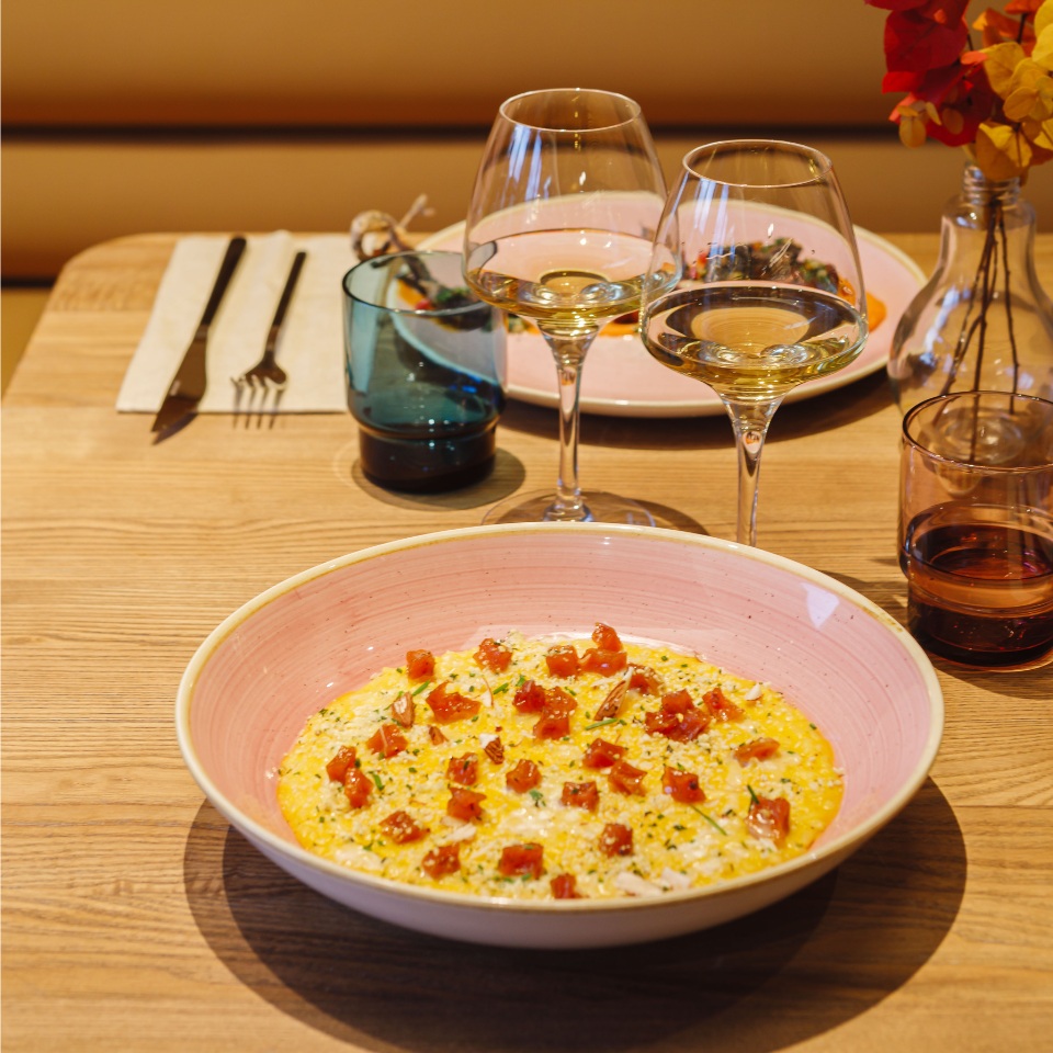A beautifully presented yellow dish garnished with diced tomatoes, surrounded by elegant glasses of white wine on a wooden table.