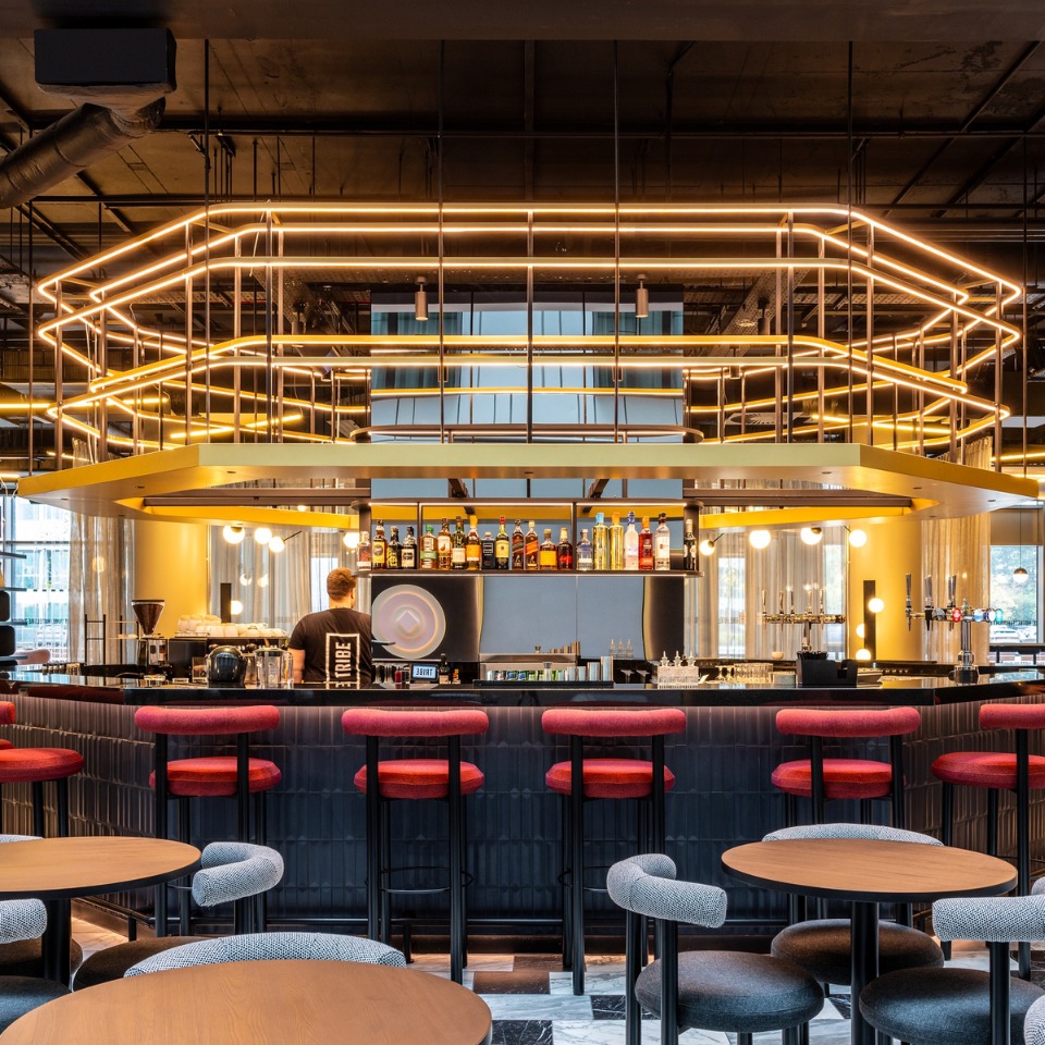 A modern bar with stylish seating, atmospheric lighting, and a bartender preparing drinks, in a contemporary lounge setting.