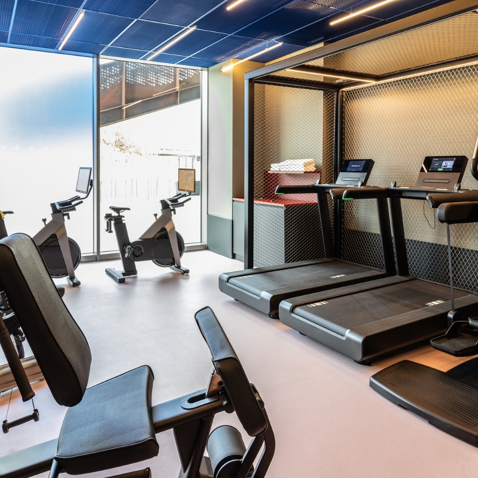 Gym interior featuring exercise bikes, treadmills, and workout equipment, illuminated by natural light from large windows.