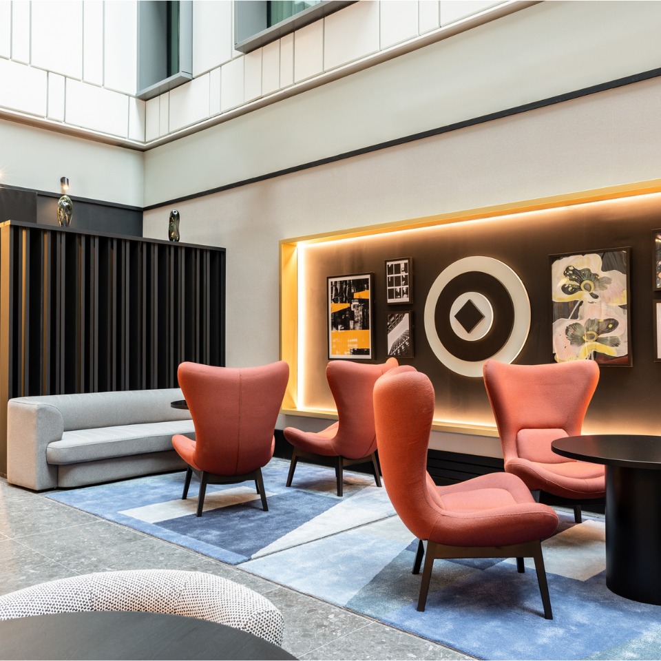 Modern lounge with orange chairs, a gray sofa, and artwork against a softly lit wall, creating a cozy ambiance.