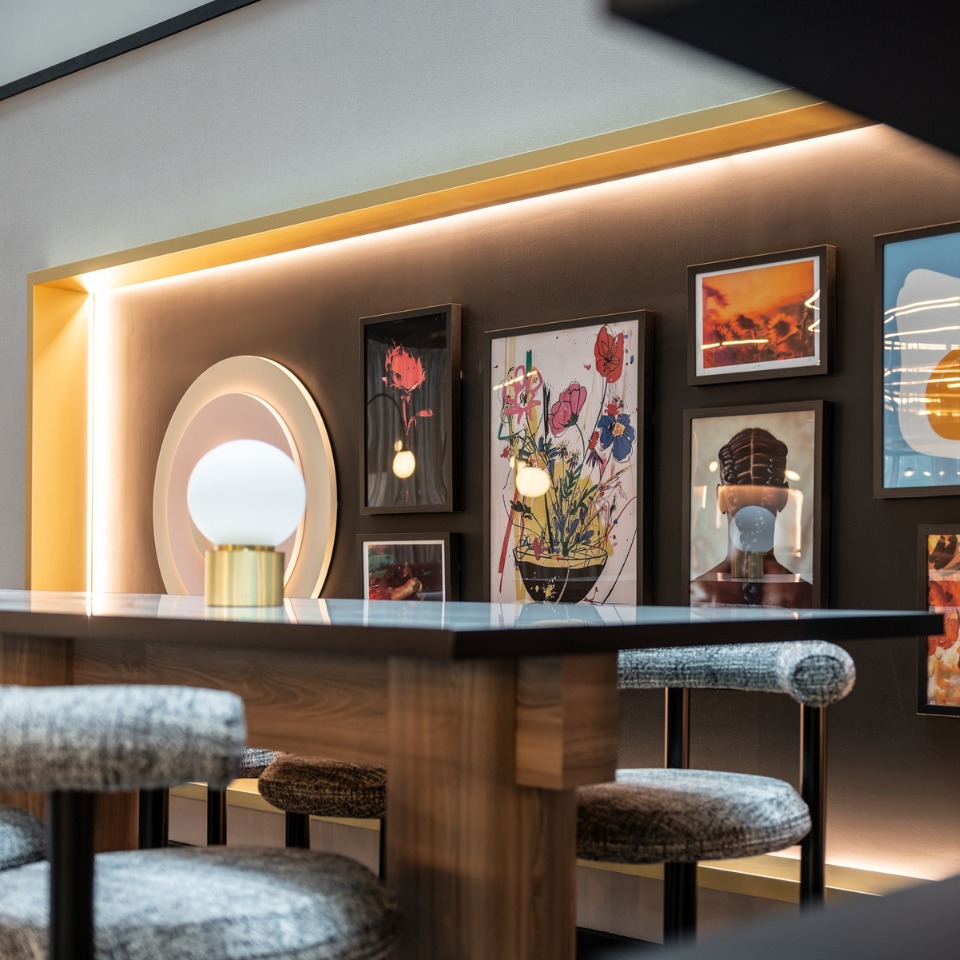A a sleek table and upholstered stools, featuring colorful artwork and warm lighting on the wall behind.