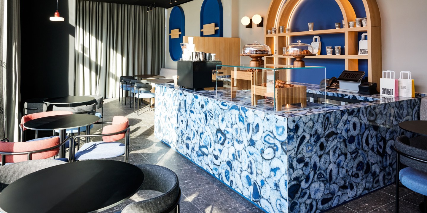 Modern cafe with a vibrant blue marble counter, a coffee station, and stylish seating illuminated by natural light.