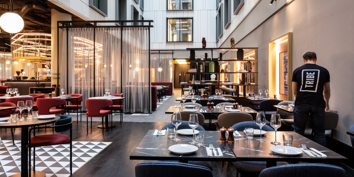 Restaurant with modern decor, featuring round tables, glassware, and a cozy ambiance enhanced by soft lighting and elegant textiles.