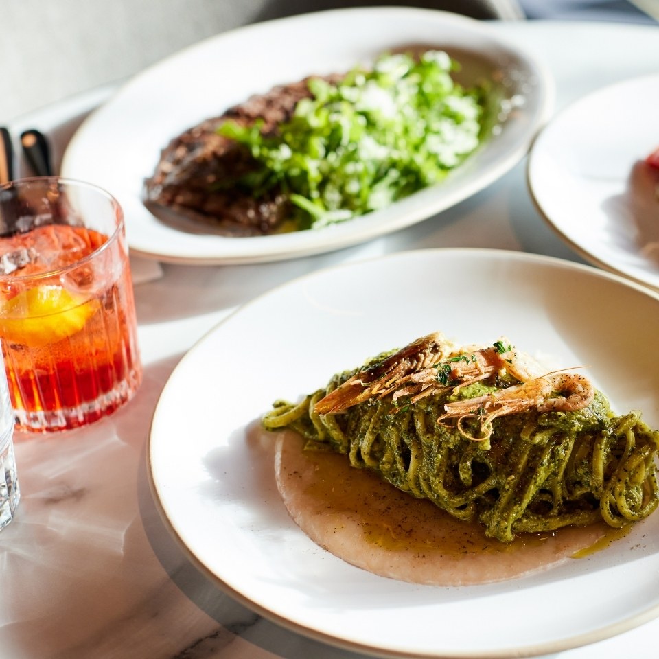 Pasta with green pesto and fish on a white plate.