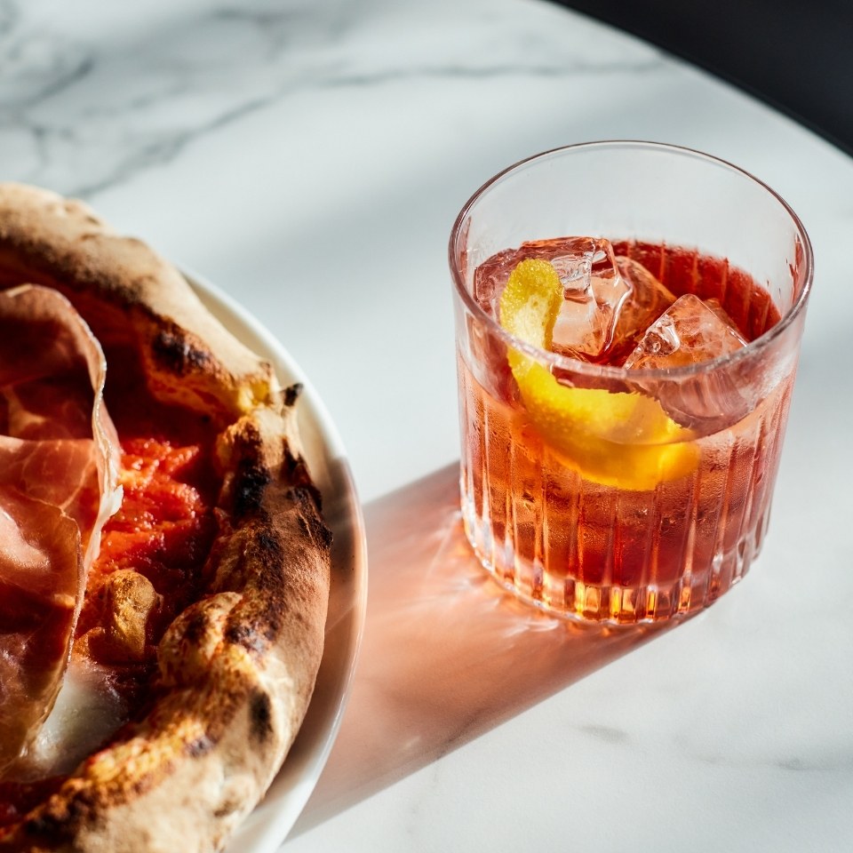 A drink with ice and a prosciutto pizza.