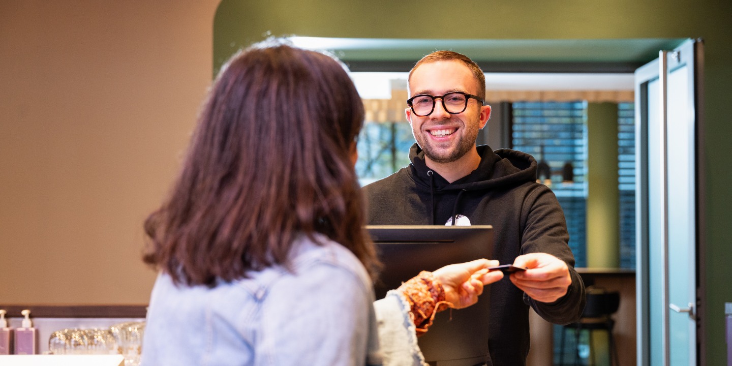A guest at a modern reception desk hands a card to a staff member, highlighting a transaction in a welcoming atmosphere.