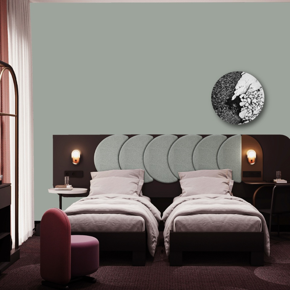 Modern hotel room with two twin beds, soft grey headboard, minimalist decor, and a round artwork, featuring a pink accent chair.