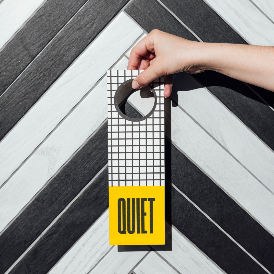 A hand holds a modern "Quiet" door hanger against a stylish black and white patterned background.
