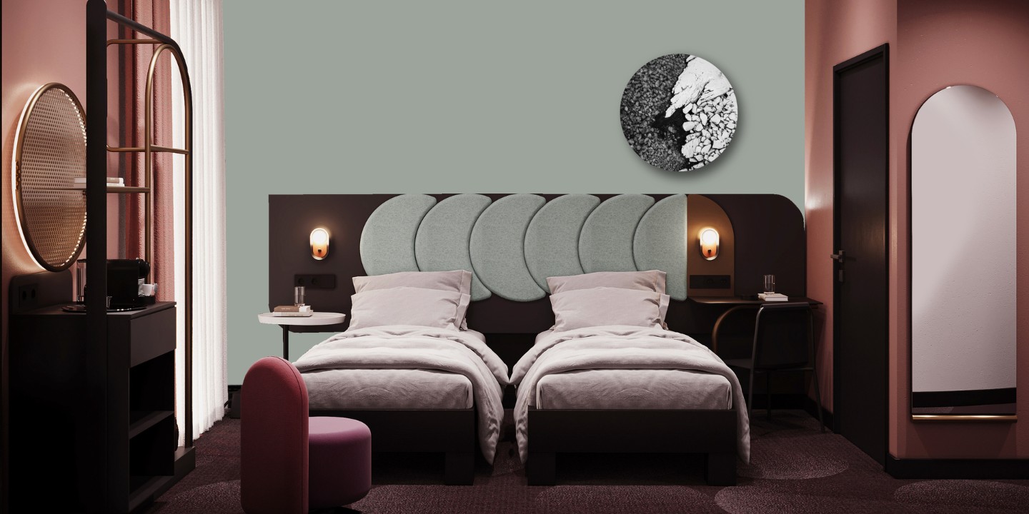 Modern hotel room with two twin beds, soft grey headboard, minimalist decor, and a round artwork, featuring a pink accent chair.