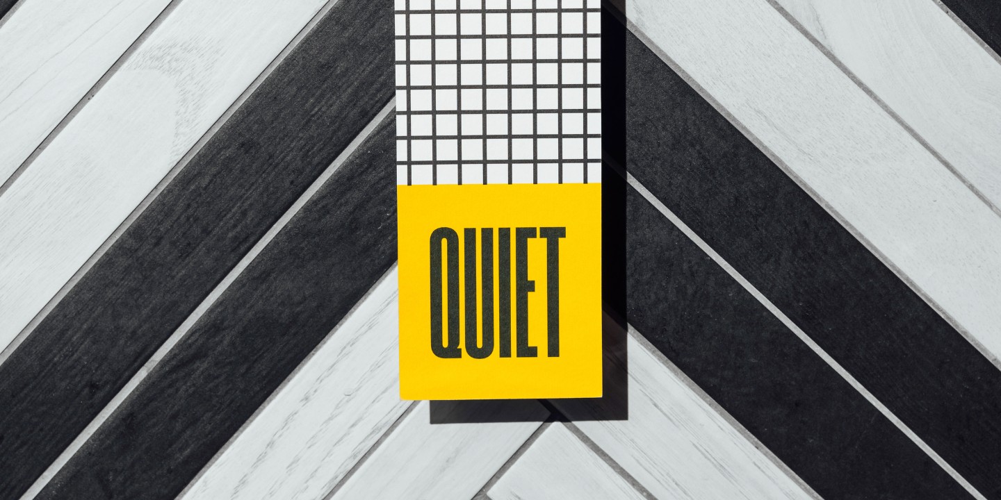 A hand holds a modern "Quiet" door hanger against a stylish black and white patterned background.