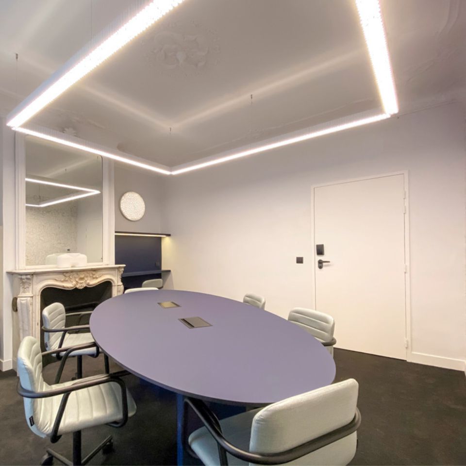 A meeting room with a large blue table and 5 chairs around it, in the background is a parisian-style fireplace