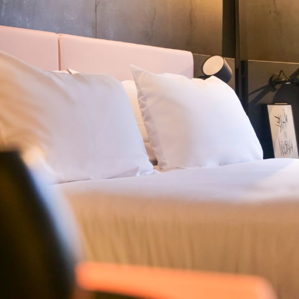 A double bed with white linen and a pink headboard