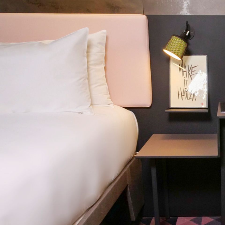A bed with a pink headboard, to the right is a nightstand with a framed picture
