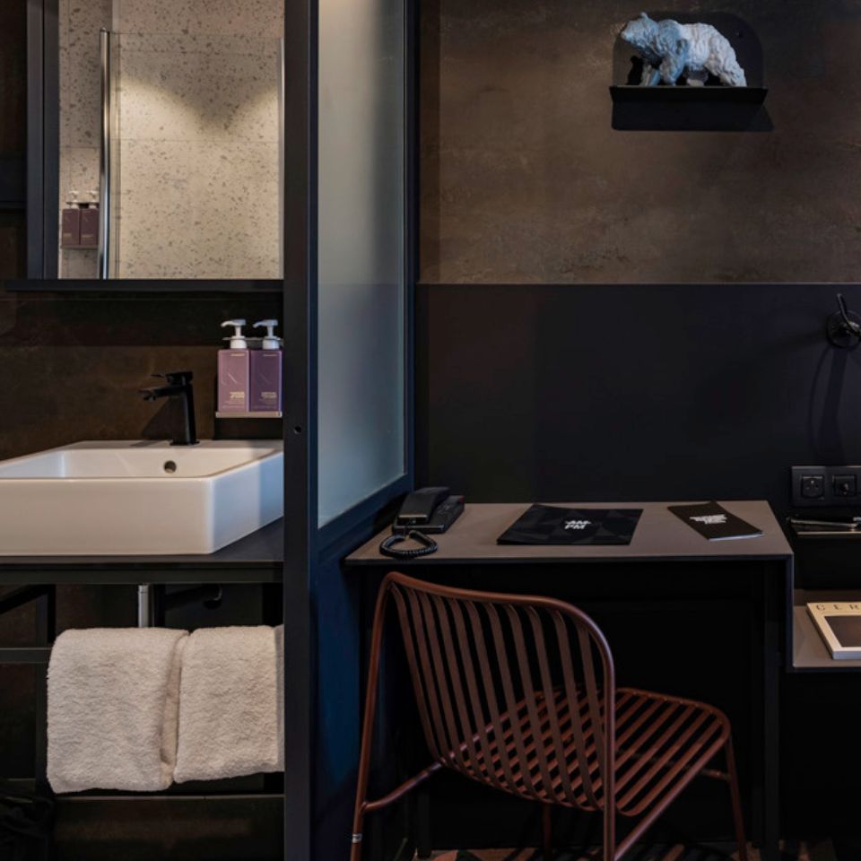 A washbasin and a mirror next to a small, black desk and a chair