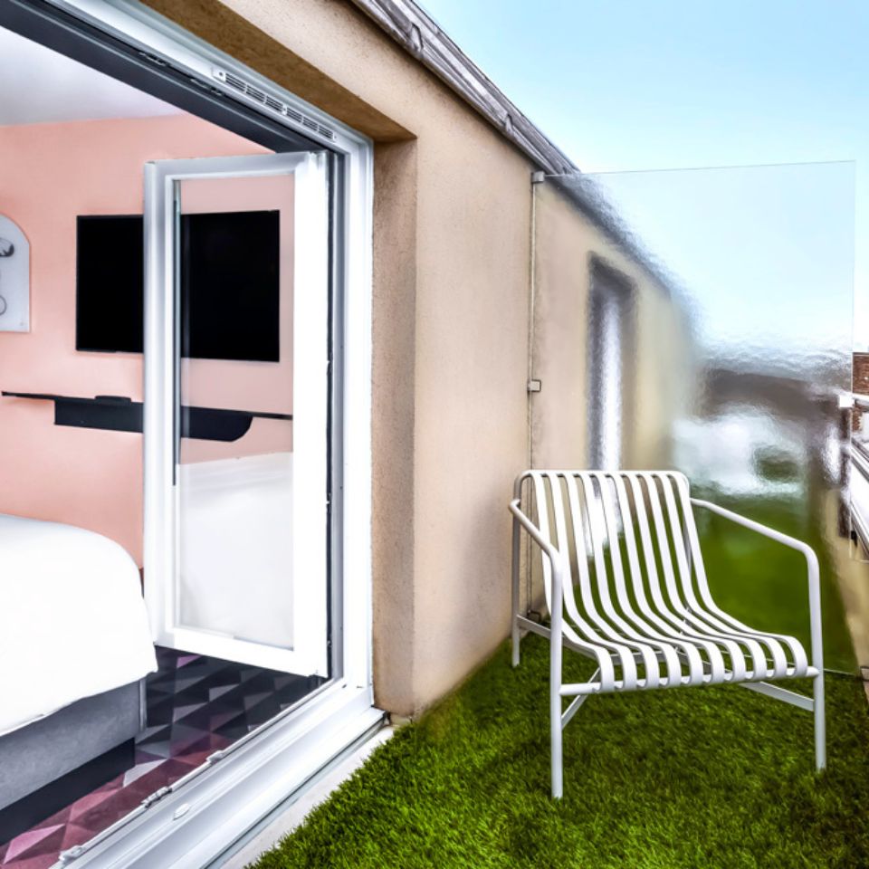 A balcony with a white chair, to the left is an open terrace door to a guest room