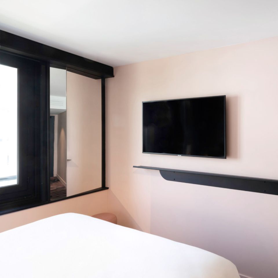 A pink wall with a black shelf and a black TV mounted to the wall