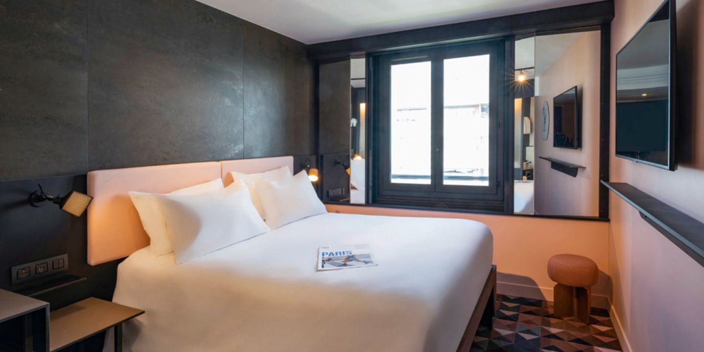 A guest room with a double bed with a pink headboard in front of a black wall