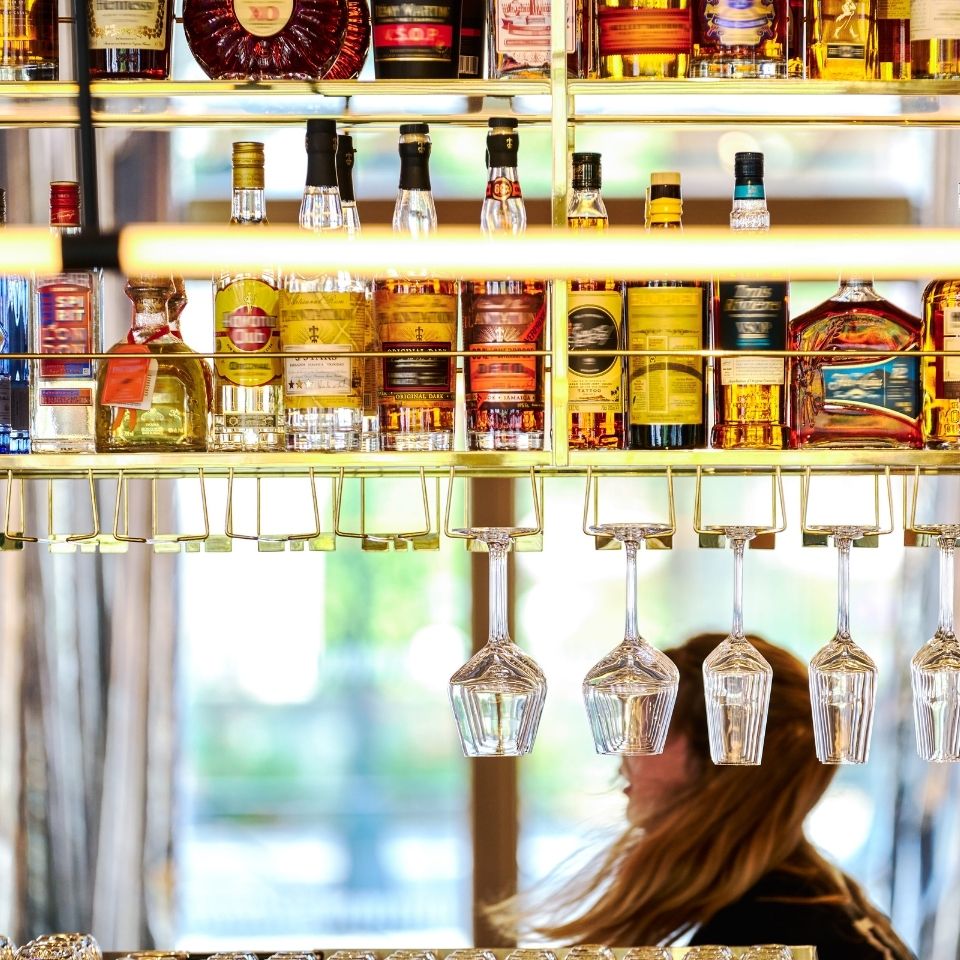 A well-stocked bar featuring an array of colorful liquor bottles arranged neatly on shelves, with glassware hanging below.