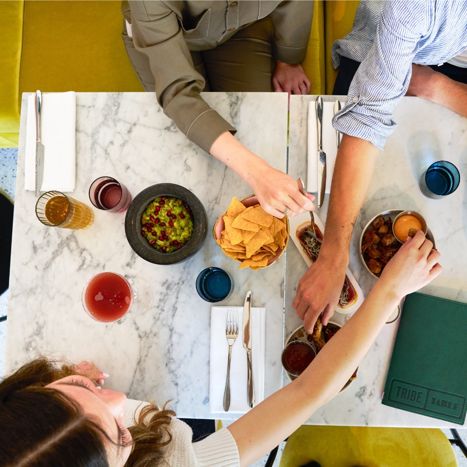 A vibrant dining table with plates of guacamole, chips, and drinks, as friends share food and enjoy their meal together.