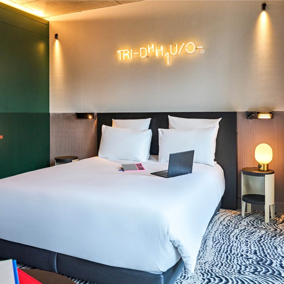 Hotel room featuring a large bed with white linens, a laptop on the bedside, and stylish lighting decor.