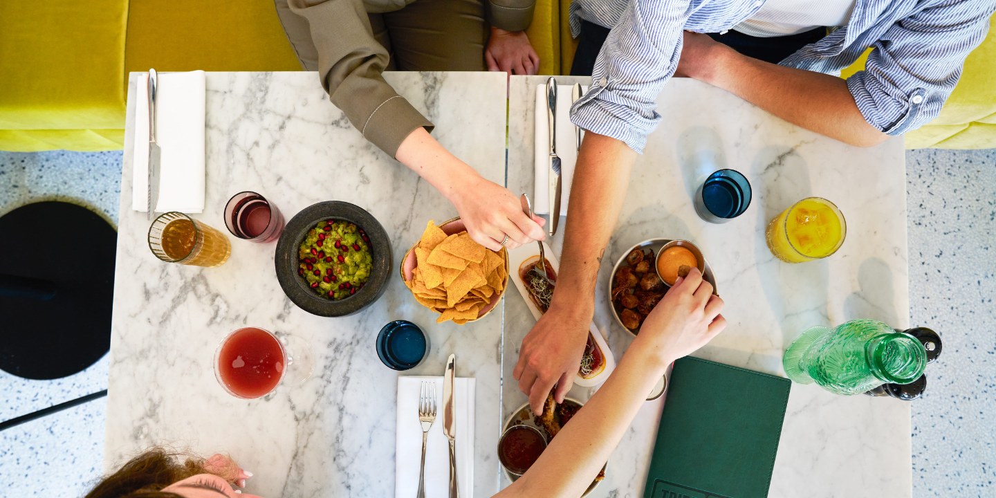 A vibrant dining table with plates of guacamole, chips, and drinks, as friends share food and enjoy their meal together.