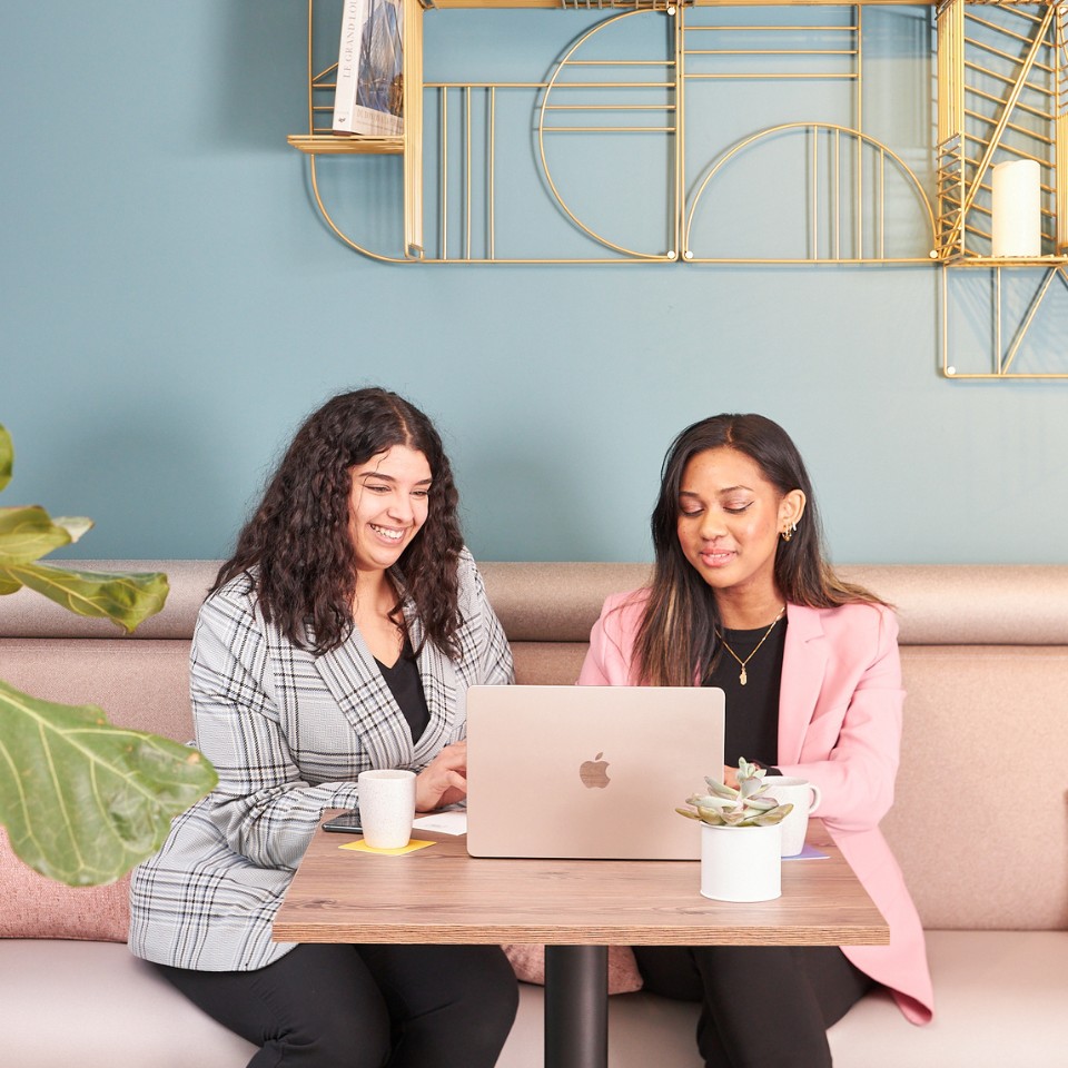 Two woman sitting on a couch lookibng at a laptop