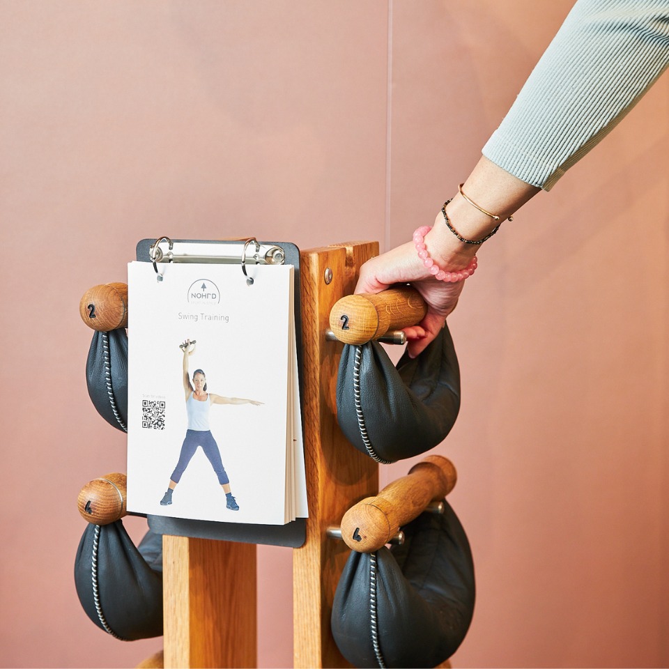 A hand reaching for a weight attached to a wooden stand with a swing training guide displayed in the background.