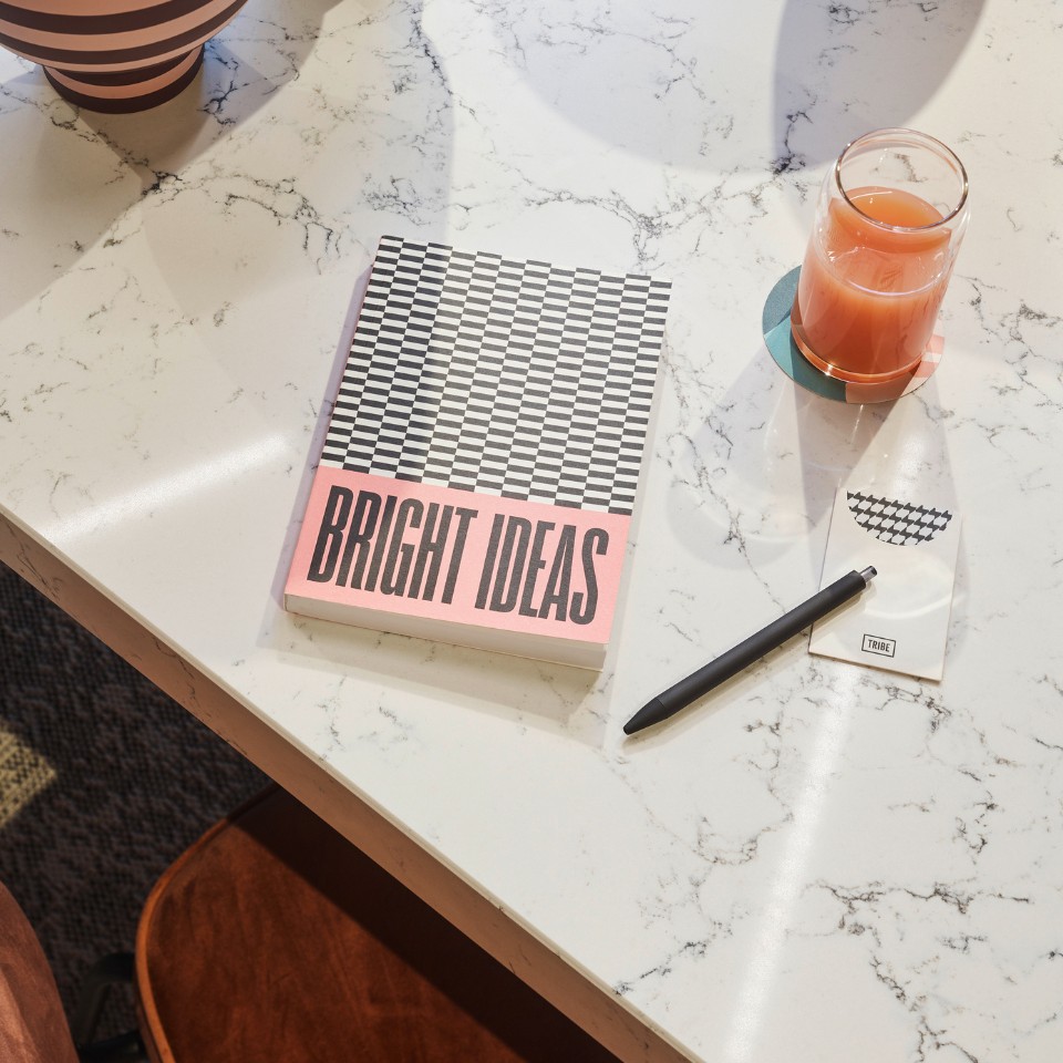 A notebook with "Bright ideas" written on it, a glass of juice and a pen on a marble table