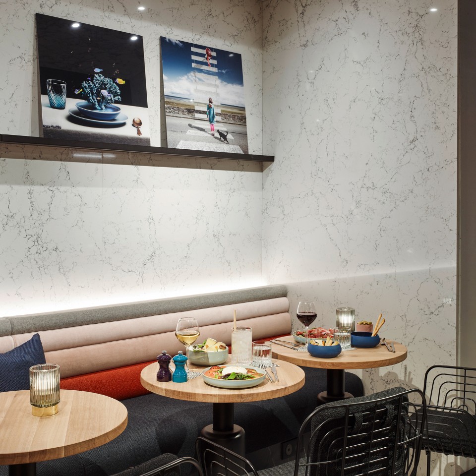 Small wooden tabled with chairs and a couch around it, there are several drinks and food on the tables